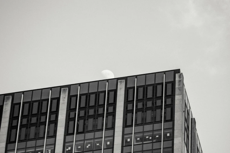 a black and white photo of a building with a moon in the sky, unsplash, brutalism, modern high sharpness photo, office building, set photo, mid shot photo
