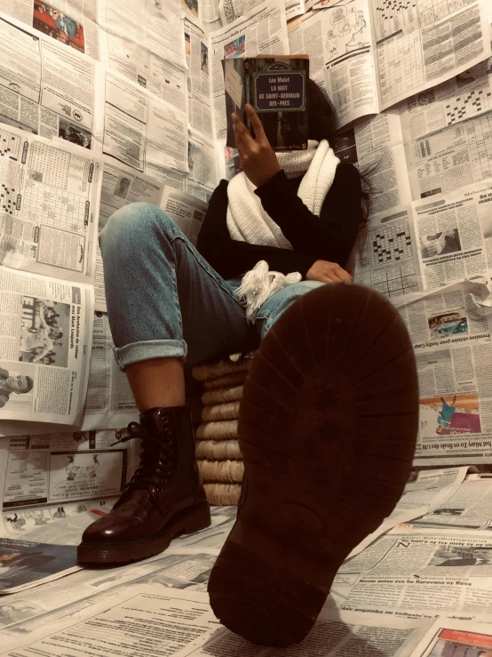 a woman sitting on a pile of newspapers reading a book, by Bernie D’Andrea, trending on reddit, wearing boots, dark skinned, low quality photo, pov photo