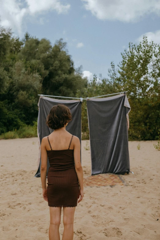 a woman standing on top of a sandy beach, an album cover, by Attila Meszlenyi, temporary art, made of fabric, near forest, low quality photo, spying