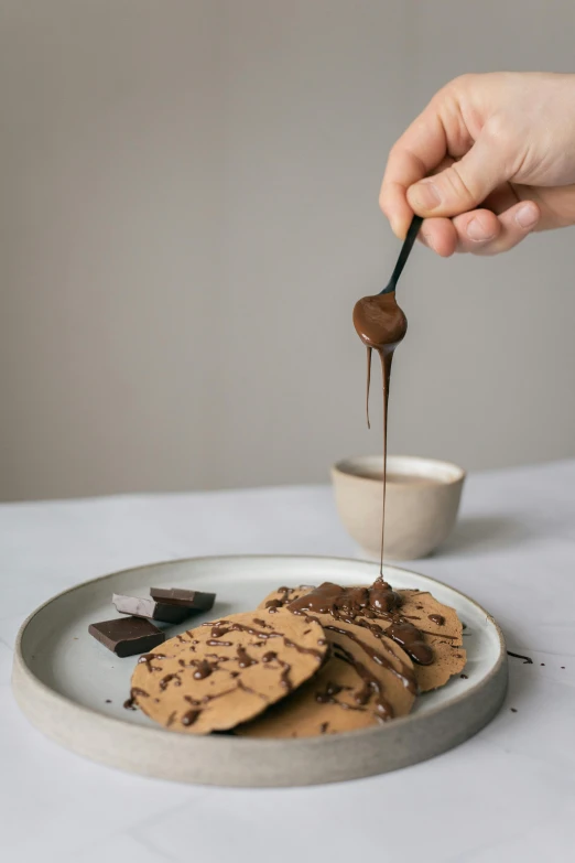 a person dipping chocolate onto a plate of cookies, inspired by Richmond Barthé, pancake flat head, spatula, full product shot, grey