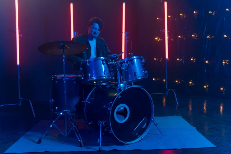 a man sitting on top of a drum kit, cinematic blue lighting, tv show still, b - roll, perfect location lighting
