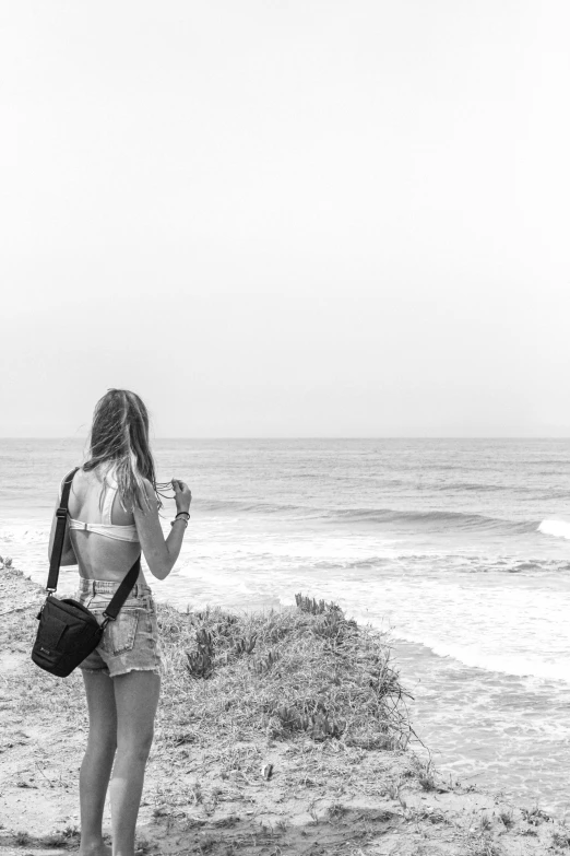 a woman standing on top of a beach next to the ocean, a black and white photo, unsplash, with a backpack, surf, panoramic view of girl, medium format