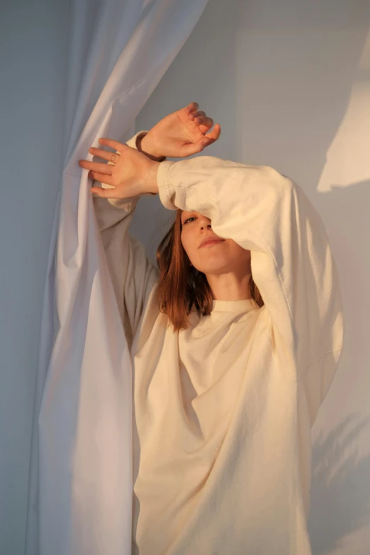 a woman standing in front of a white curtain, an album cover, inspired by Anna Füssli, aestheticism, hands shielding face, long shirt, morning glow, ignant