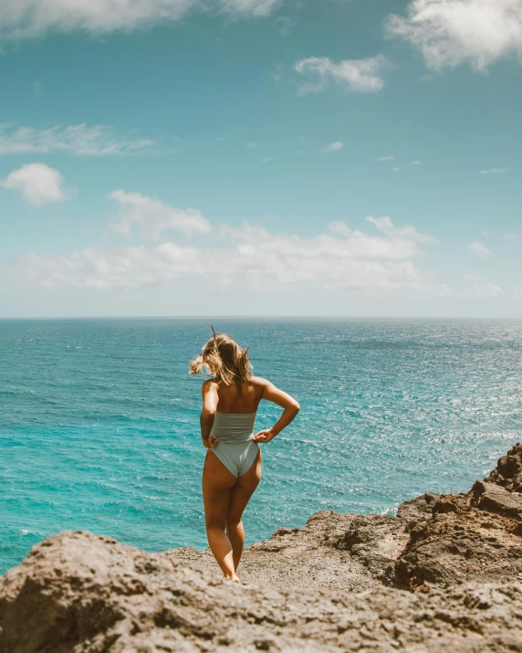 a woman standing on top of a cliff next to the ocean, sparky swimsuit, profile image, hawaii beach, 2019 trending photo