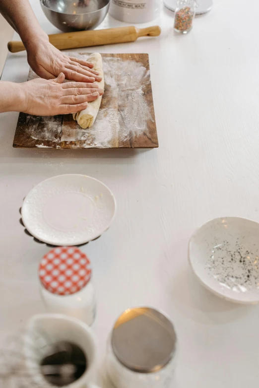 a woman is rolling out dough on a table, a still life, inspired by Josefina Tanganelli Plana, trending on unsplash, made of glazed, white, panoramic, sparkling