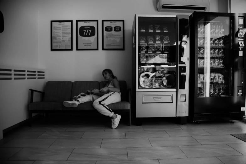 a woman sitting on a couch next to a vending machine, a black and white photo, by Emma Andijewska, pexels contest winner, fast food, resting after a hard mission, gif, gumball machine