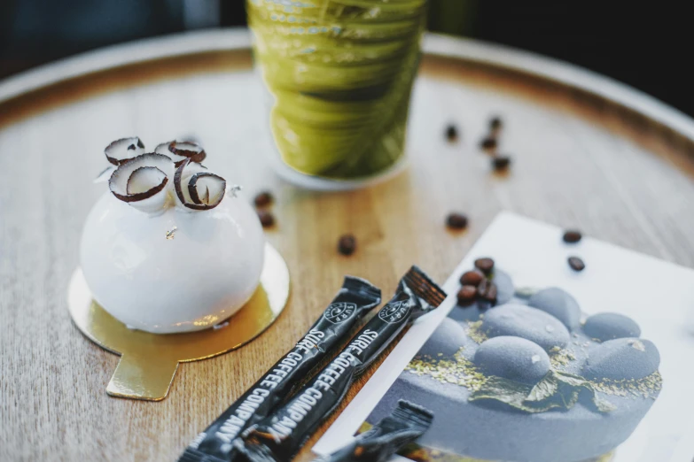 a cake sitting on top of a wooden table next to a cup of coffee, inspired by Ödön Márffy, pexels contest winner, marble and gold, avacado dream, iced latte, graphic detail