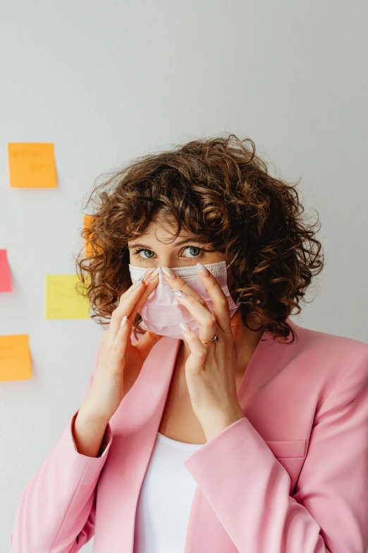 a woman standing in front of a wall covered in post it notes, a picture, pexels, surgical mask covering mouth, messy curly hair, people at work, plain background