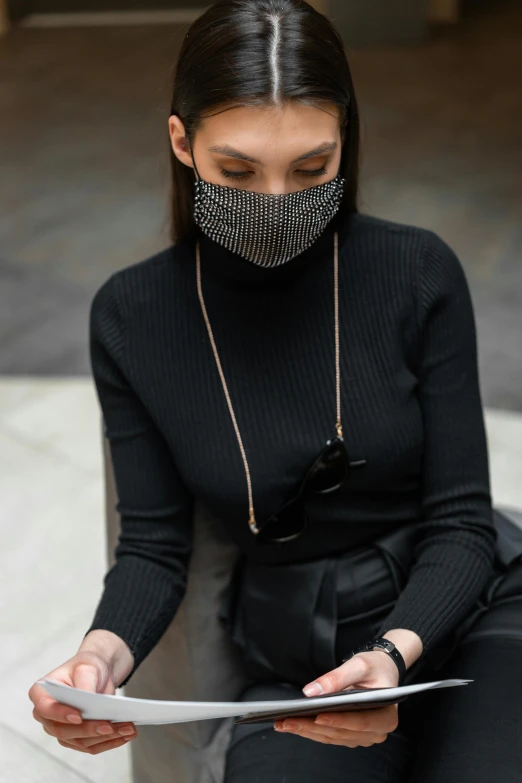 a woman sitting on a bench reading a piece of paper, a portrait, by Nina Hamnett, trending on pexels, balaclava mask, wearing a chain, black turtleneck, luxury fashion