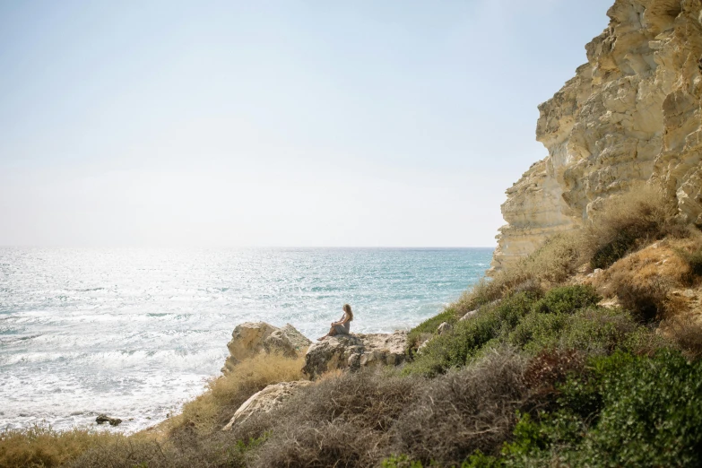 a man sitting on top of a cliff next to the ocean, by Simon Marmion, unsplash, minimalism, cyprus, amongst foliage, over a chalk cliff, profile image