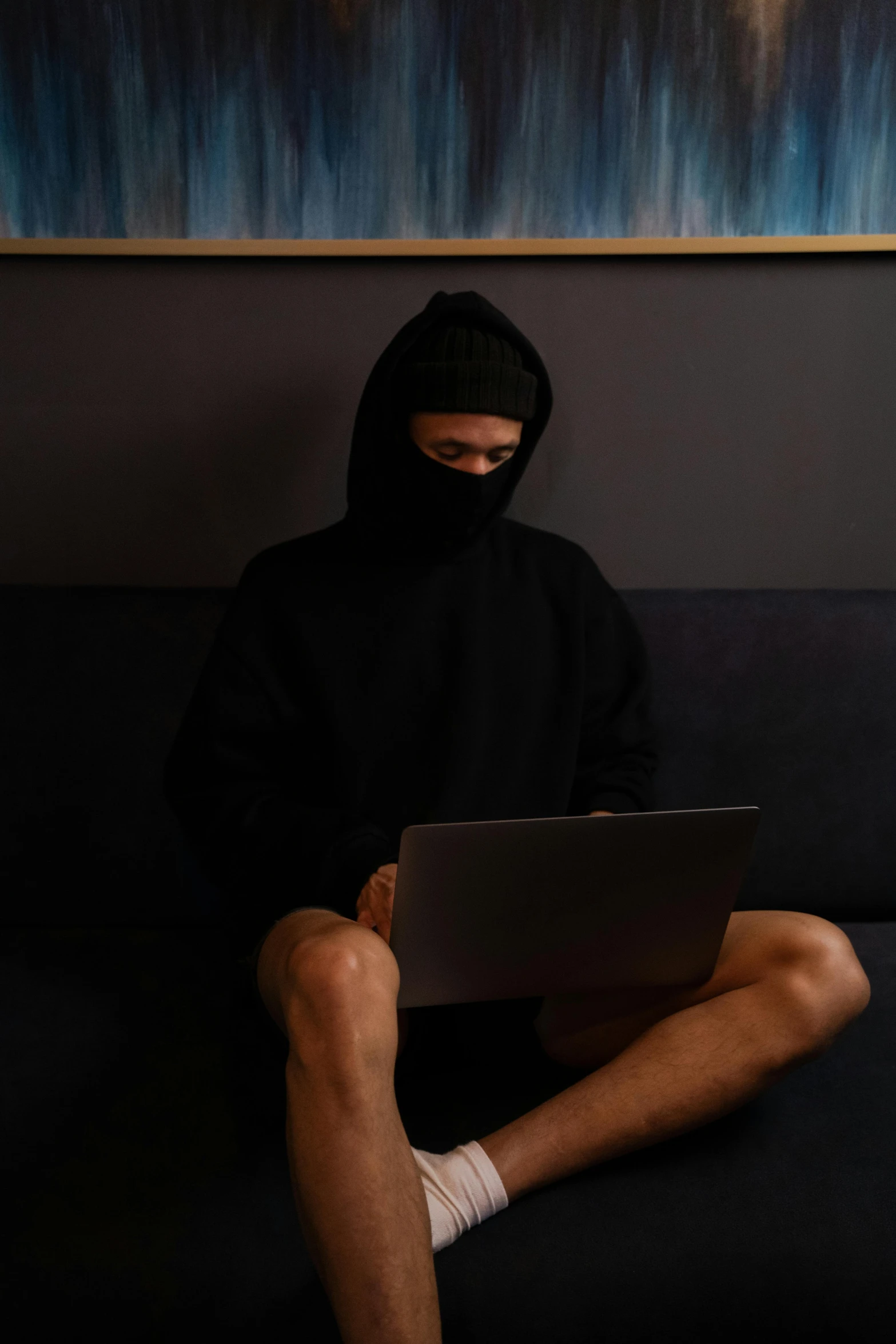 a person sitting on a couch with a laptop, black hood, wearing nothing, face covered, scumbled