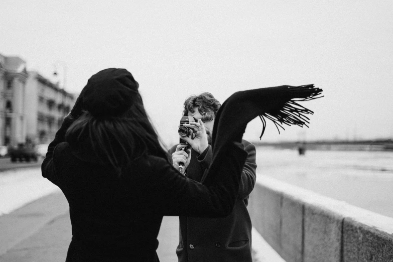 a couple of women standing next to each other, a black and white photo, by Emma Andijewska, pexels contest winner, holding a ray gun, wrapped in a black scarf, man proposing his girlfriend, video footage