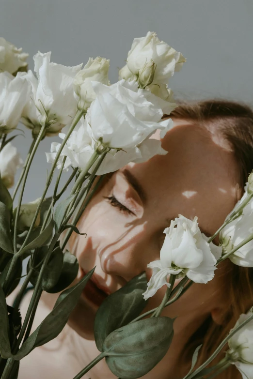 a woman holding a bunch of white flowers in front of her face, trending on unsplash, romanticism, lying down, portrait of kim petras, portrait photo, laying on roses