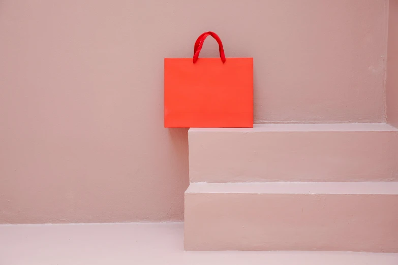 a red shopping bag sitting on top of a set of stairs, by Helen Stevenson, pexels contest winner, postminimalism, pastel pink neon, orange gi, front facing, a small