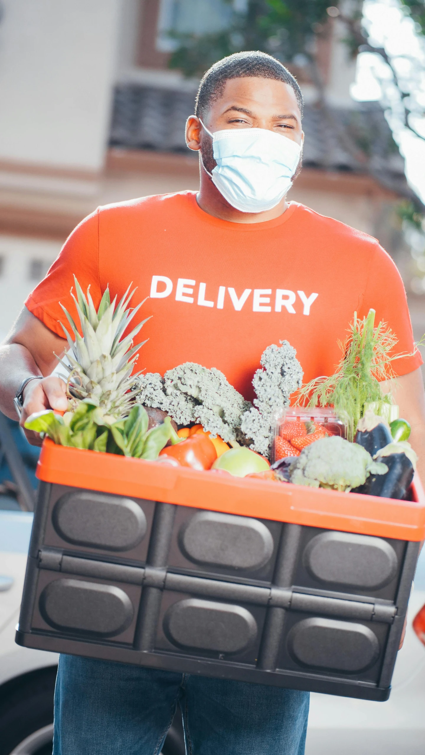 a man wearing a face mask holding a box of fruit and vegetables, a digital rendering, pexels, hurufiyya, wearing an orange t-shirt, exiting store, logo for lunch delivery, square