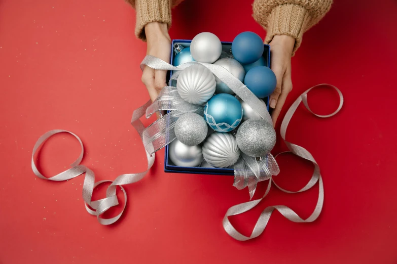 a person holding a box filled with blue and silver ornaments, pexels contest winner, plasticien, ribbon, solid colours, product shot, teal silver red