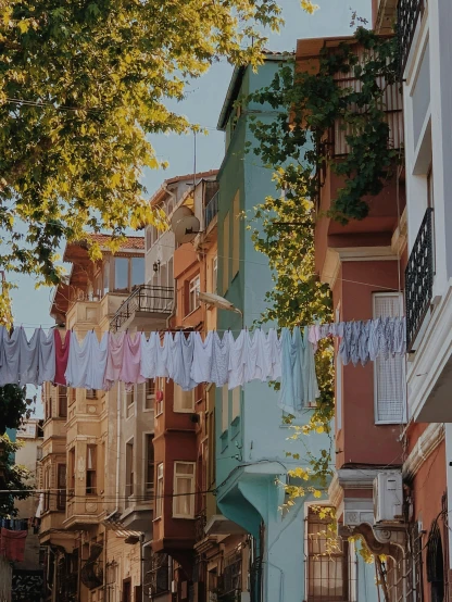 a group of people walking down a street next to tall buildings, by Matija Jama, pexels contest winner, renaissance, laundry hanging, turkish and russian, vines hanging from trees, pastel colored