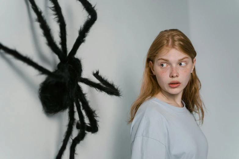 a girl standing in front of a fake spider, trending on pexels, a redheaded young woman, black eyed, teenager, indoor picture