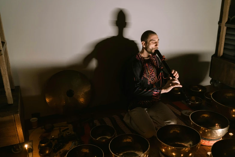 a man sitting in front of a group of singing bowls, an album cover, inspired by Aladár Körösfői-Kriesch, unsplash, light show, shadow, backdrop, performing