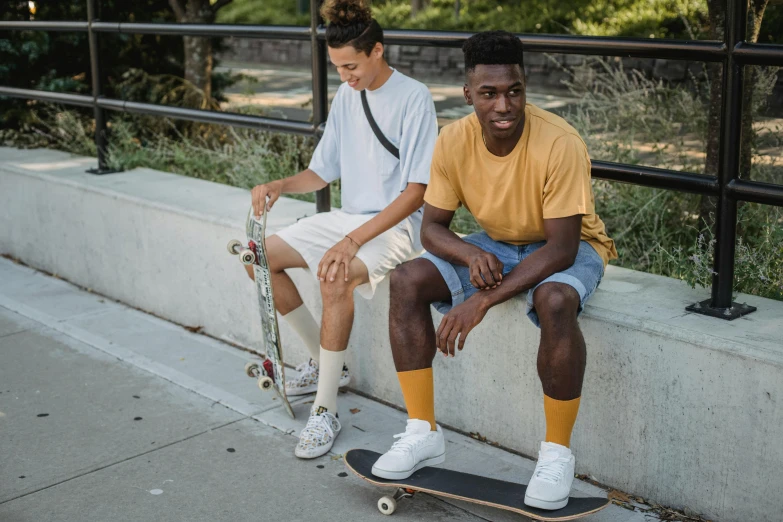 a couple of men sitting on top of a skateboard, pexels contest winner, gold soccer shorts, ( ( dark skin ) ), college students, wearing off - white style