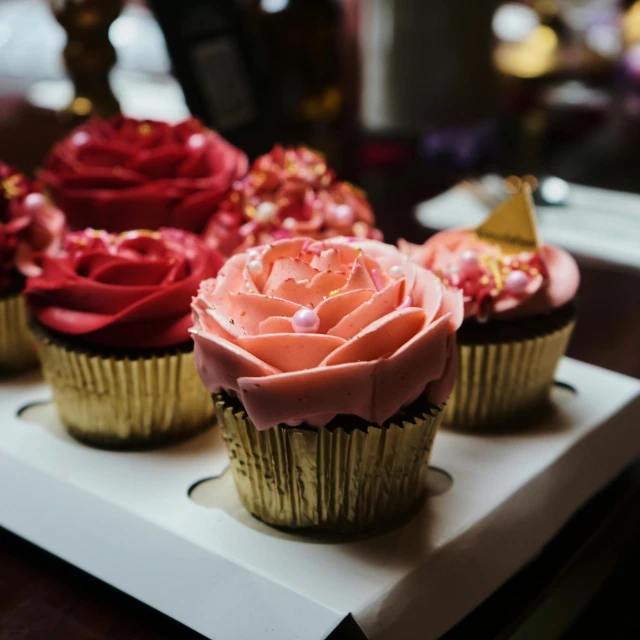 a close up of three cupcakes on a tray, pexels contest winner, roses, varying ethnicities, pink and gold, red and brown color scheme