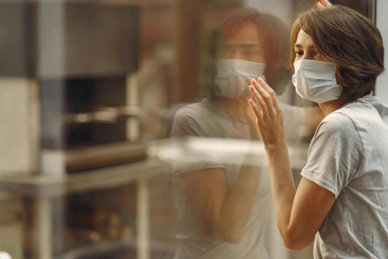 a woman wearing a face mask standing in front of a window, a picture, trending on pexels, hands shielding face, australian, people walking around, fume