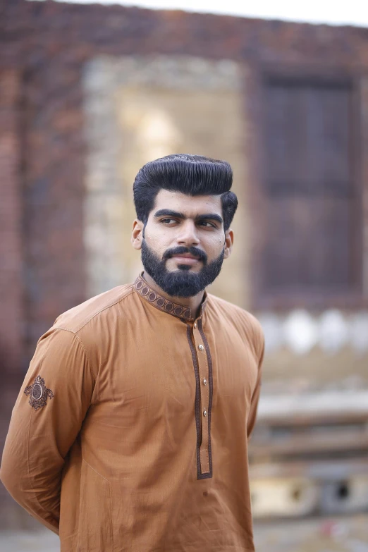 a man with a beard standing in front of a building, by Riza Abbasi, pexels contest winner, hurufiyya, with brown skin, wearing a kurta, brown:-2, handsome young man