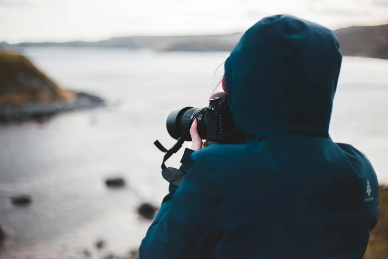 a person taking a picture of a body of water, is looking at the camera, short telephoto, looking out over the sea, professional image