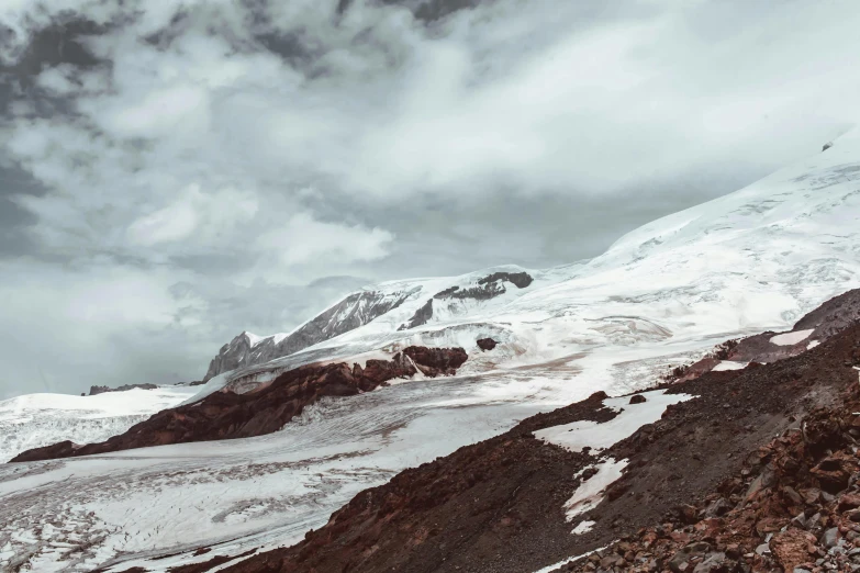 a man standing on top of a snow covered mountain, a matte painting, by Daniel Seghers, pexels contest winner, glaciers, grey skies, brown, seen from afar