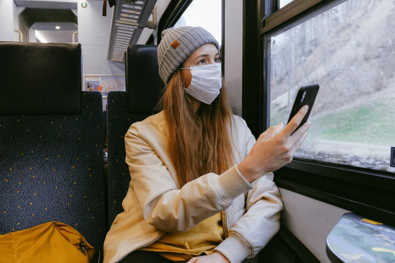 a woman sitting on a train looking at her phone, trending on pexels, medical mask, avatar image, ski masks, public bus