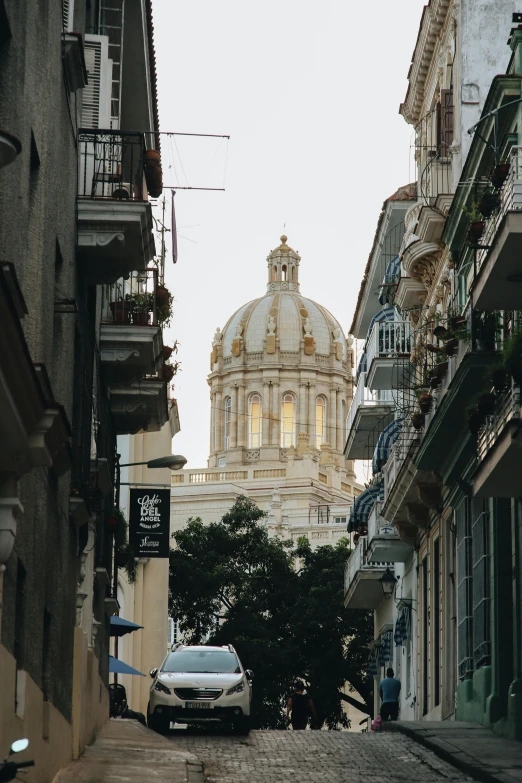 a car is parked on a cobblestone street, by Matteo Pérez, trending on unsplash, neoclassicism, neoclassical tower with dome, outdoors tropical cityscape, view from back, color image