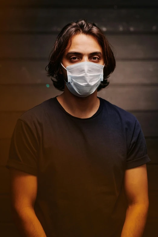 a man wearing a face mask with his hands in his pockets, an album cover, trending on pexels, low key lights, mid long hair, medical mask, greg rutowski