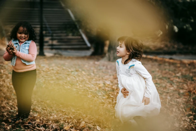 a couple of little girls standing next to each other, pexels contest winner, happening, wind blows the leaves, girl is running, sydney park, 15081959 21121991 01012000 4k