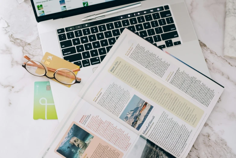 a laptop computer sitting on top of a table next to a book, a picture, travel guide, magazine pages, knolling, educational supplies