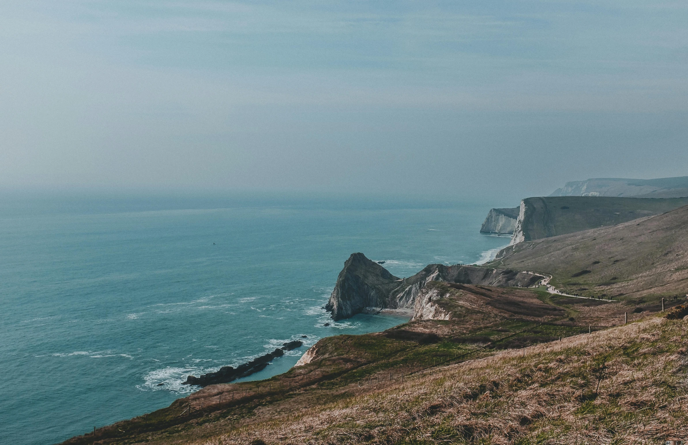 a person standing on top of a hill next to the ocean, by Nick Fudge, pexels contest winner, renaissance, chalk cliffs above, teal color graded, thumbnail, hills and ocean