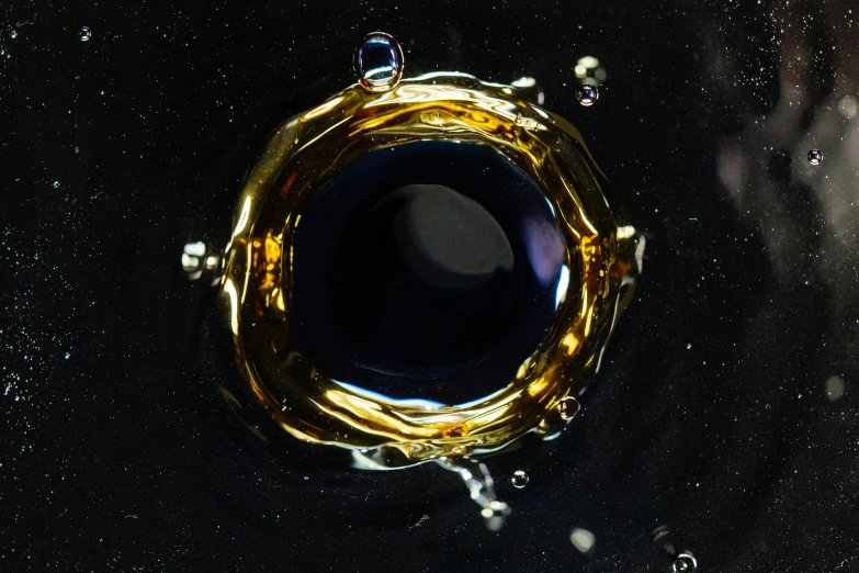 a close up of a glass with a liquid inside of it, an album cover, inspired by Otto Piene, unsplash, black gold color scheme, black hole in space, gold and indigo, made of liquid metal