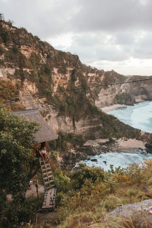 a man standing on top of a cliff next to the ocean, bamboo huts, swinging on a vine over a chasm, flatlay, 2019 trending photo