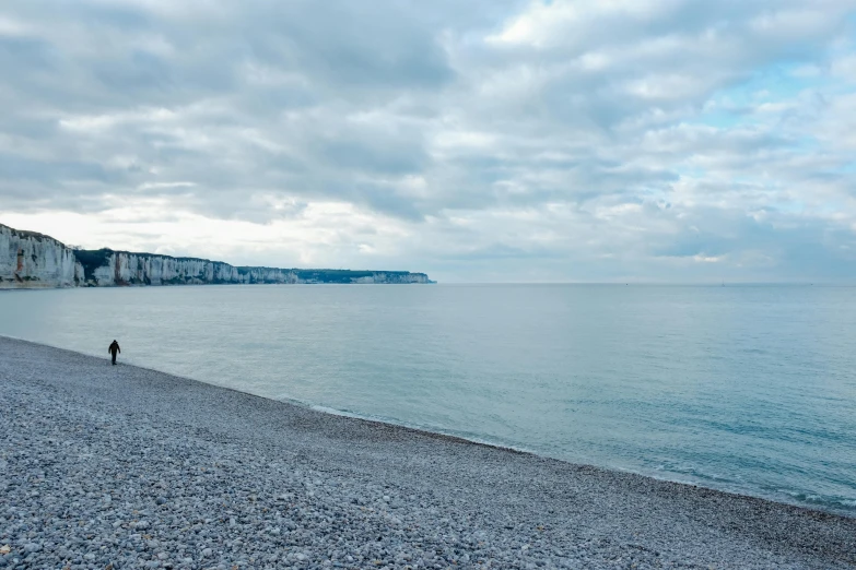 a person standing on a beach next to a body of water, inspired by Thomas Struth, unsplash, cliffs of dover, overcast sky, picton blue, today\'s featured photograph 4k