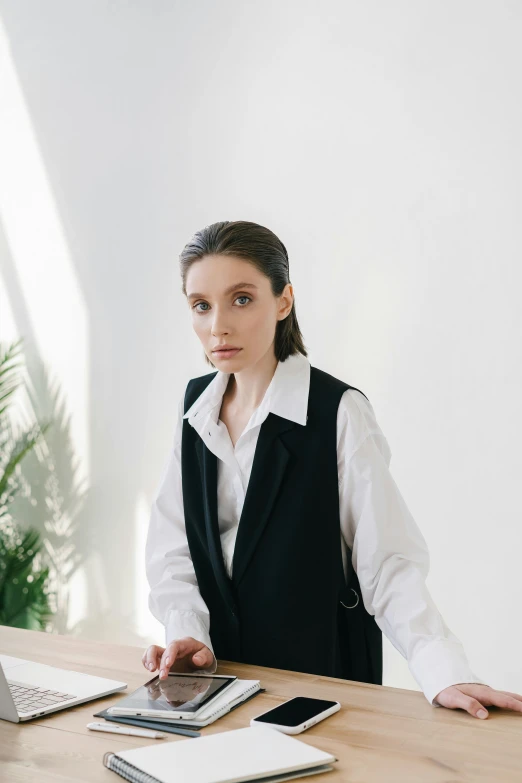 a woman sitting at a desk in front of a laptop computer, a character portrait, inspired by Anna Füssli, trending on pexels, renaissance, suit vest, in a white room, portrait androgynous girl, girl standing