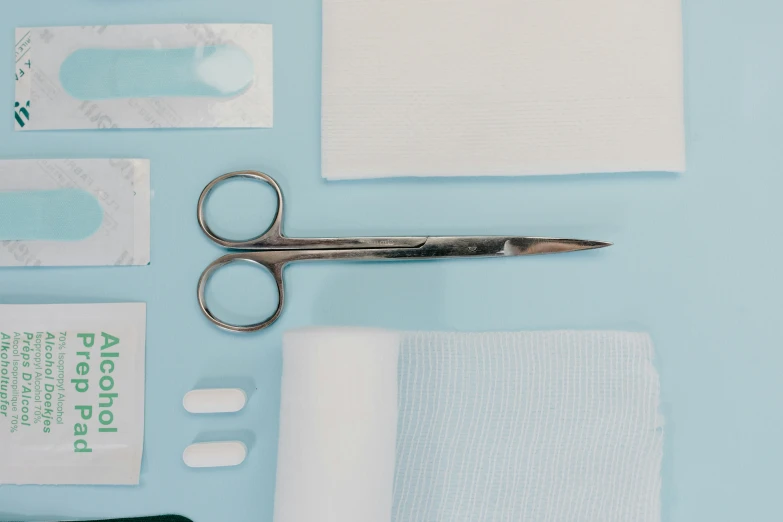 a pair of scissors sitting on top of a table, by Helen Stevenson, trending on pexels, happening, first aid kit, white and pale blue, surgeon, layered composition