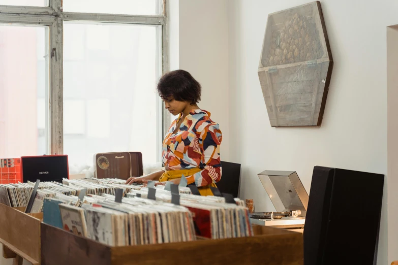 a woman standing in front of a table full of records, unsplash, private press, brown, facing sideways, music being played, at checkout