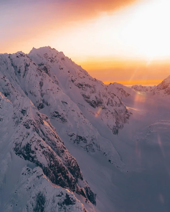 a person standing on top of a snow covered mountain, in the sunset