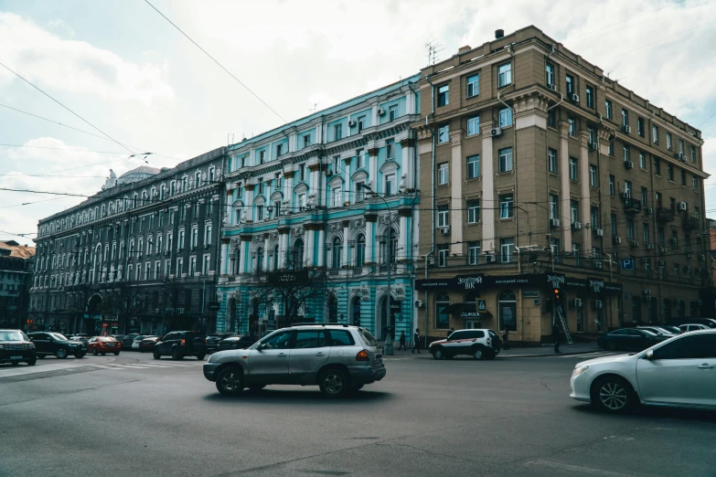 a group of cars driving down a street next to tall buildings, a photo, pexels contest winner, neoclassicism, khreschatyk, brown and cyan color scheme, 000 — википедия, old building