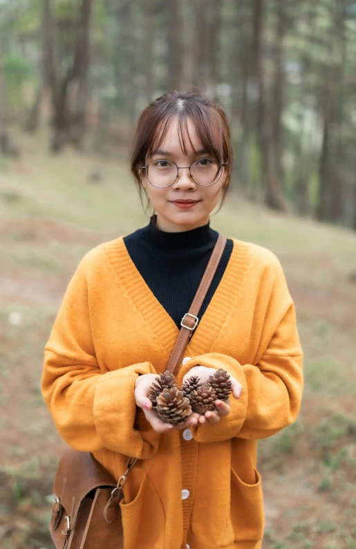 a woman holding a pine cone in her hands, a portrait, inspired by Li Fangying, pexels contest winner, wearing casual sweater, avatar image, tourist photo, malaysian