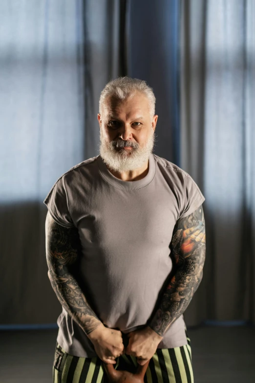 a man standing with his hands in his pockets, a tattoo, inspired by Lajos Vajda, greybeard, wearing a muscle tee shirt, photo from a promo shoot, photograph taken in 2 0 2 0