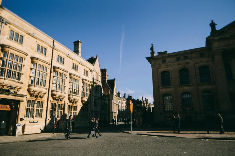 a group of people walking across a street next to tall buildings, pexels contest winner, academic art, medieval architecture, bath, clear sunny day, old library