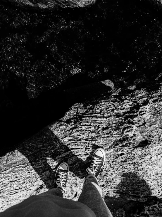 a black and white photo of a person standing on a rock, realism, high angle vertical, sneaker photo, long shadow, low-angle