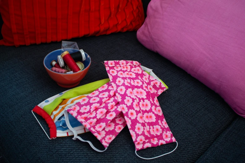 a pair of mitts sitting on a couch next to a bowl of crayons, by Rachel Reckitt, pexels, surgical mask covering mouth, wearing pink floral chiton, cushions, detail shot