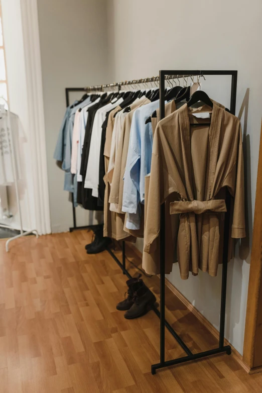 a rack of clothes sitting on top of a wooden floor, wearing brown robes, light brown coat, storefront, clean image