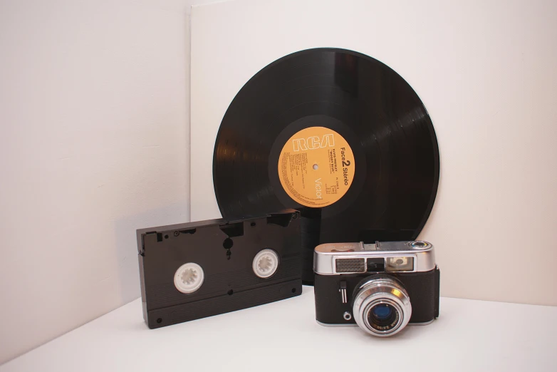 a camera sitting on top of a table next to a record, an album cover, vhs artefacts, 4k museum photograph, high quality product image”, studio medium format photograph